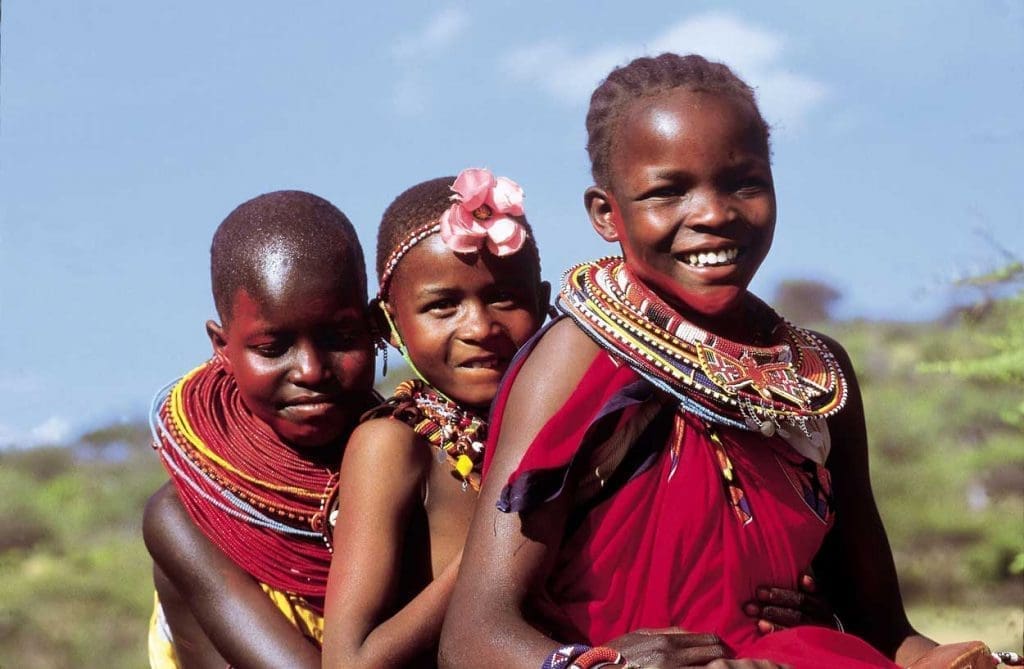 A group of joyful Maasai children with beaming smiles, wearing vibrant traditional clothing, enjoying a Tanzania safari adventure amidst the stunning natural beauty of the grasslands