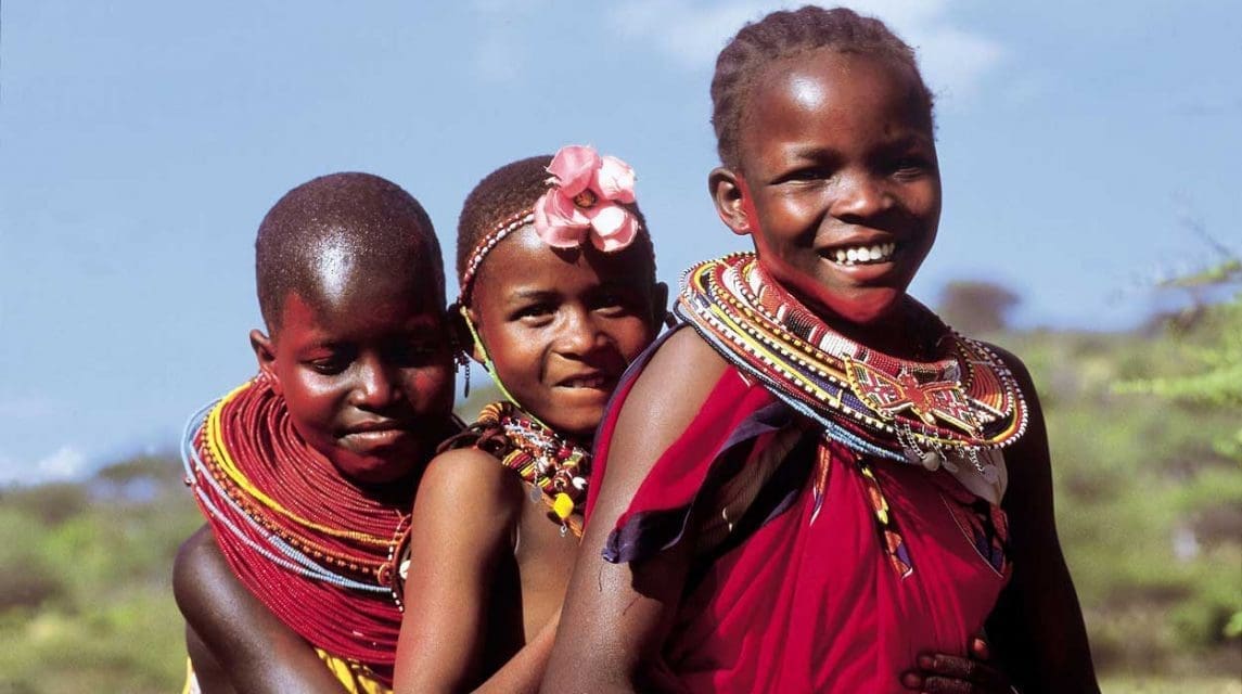 A group of joyful Maasai children with beaming smiles, wearing vibrant traditional clothing, enjoying a Tanzania safari adventure amidst the stunning natural beauty of the grasslands