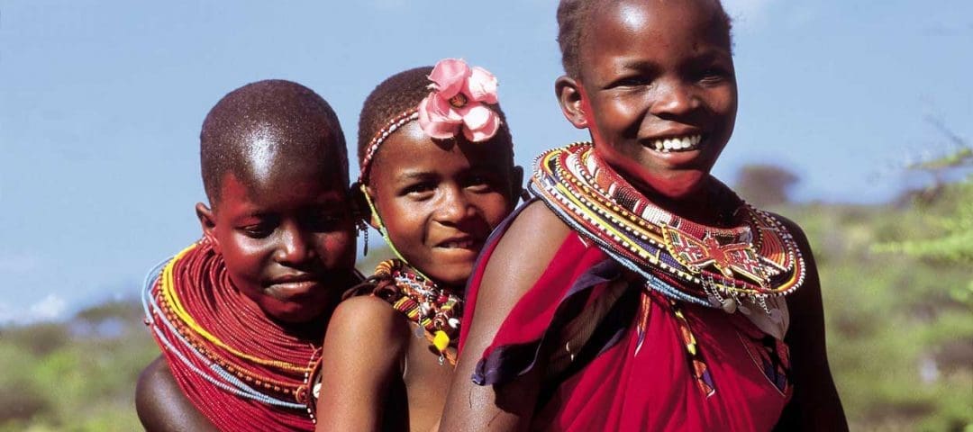 A group of joyful Maasai children with beaming smiles, wearing vibrant traditional clothing, enjoying a Tanzania safari adventure amidst the stunning natural beauty of the grasslands